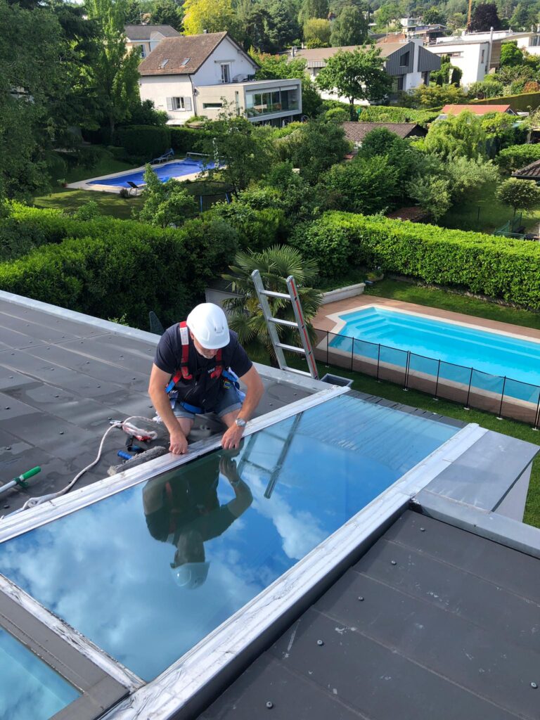 Un spécialiste de Vitre et Clair SA réalise l'entretien professionnel d'un panneau solaire sur un toit à Genève, service certifié disponible à la vente et livraison.