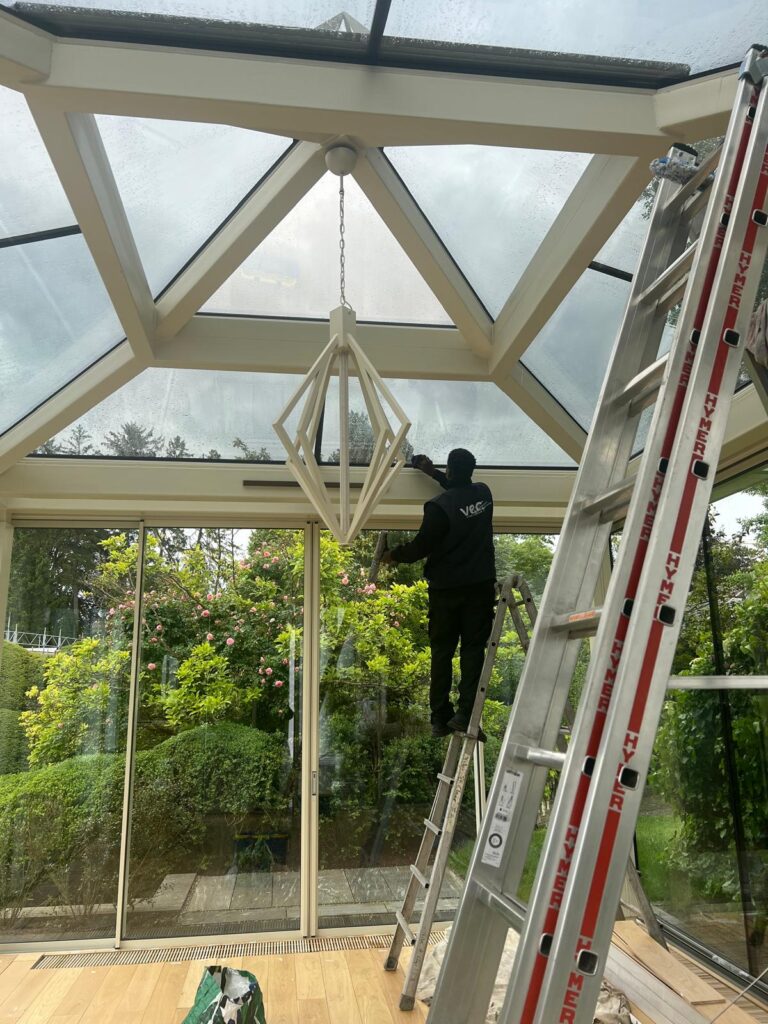 Professionnel du nettoyage Vitre et Clair assurant l'entretien de vitres dans une véranda lumineuse à Genève, avec équipement spécialisé et échelle.