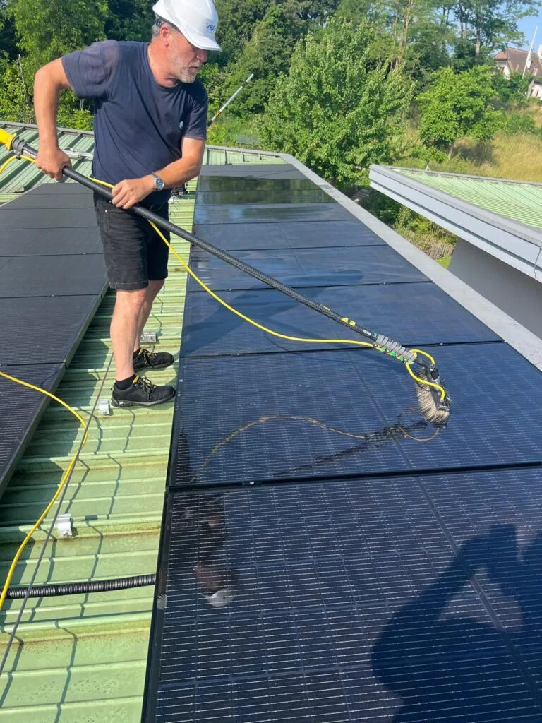Technicien de Vitre et Clair effectuant le nettoyage professionnel de panneaux solaires sur un toit à Genève, avec équipement certifié pour un entretien efficace.